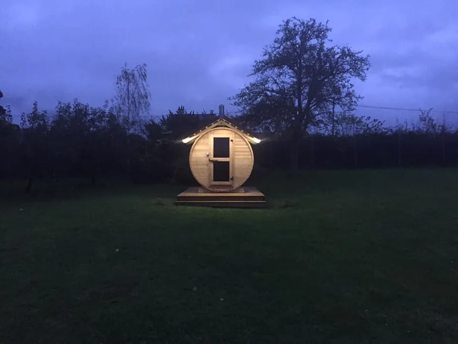 Beleuchtete Fasssauna im Garten in der Abenddämmerung